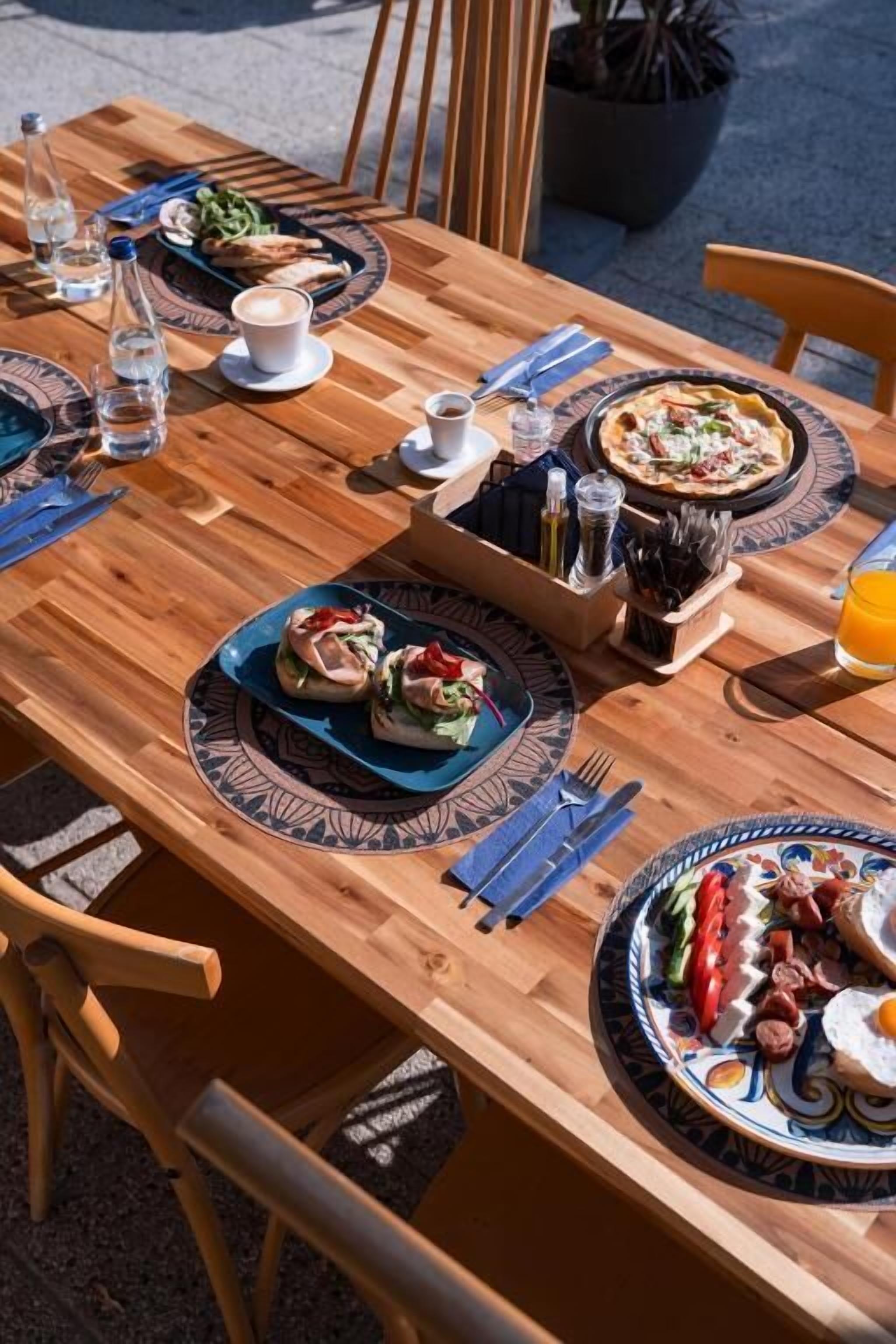 A wooden dining table with plates of food, glasses, and cutlery.