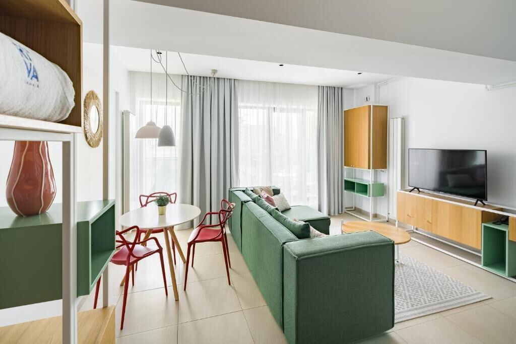 Una sala de estar moderna con un sofá verde, sillas rojas, una mesa de comedor y un televisor.