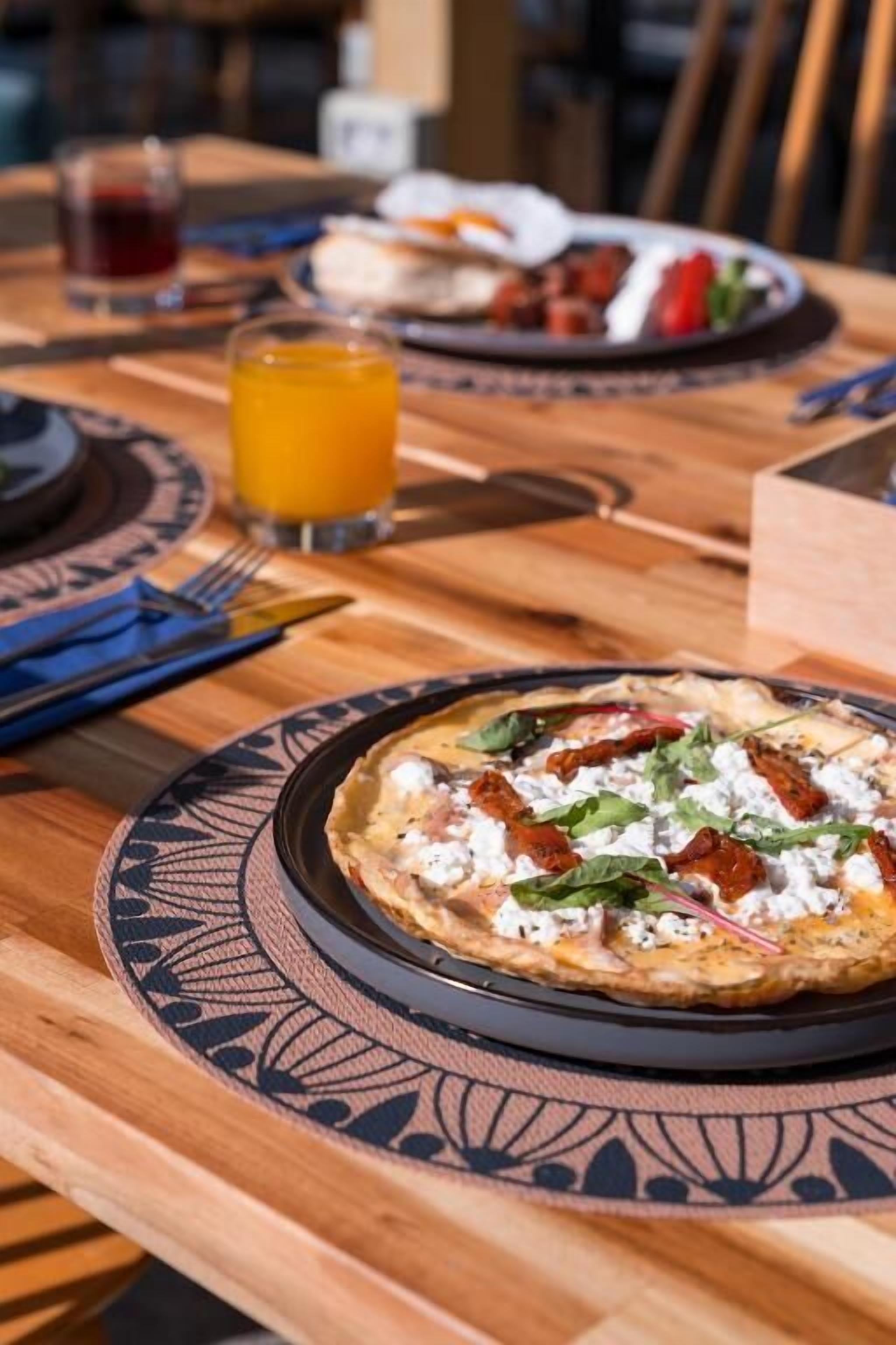 Een eettafel met een bord eten, een glas sinaasappelsap en een vork.