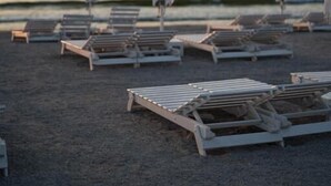 A beach with rows of sun loungers and umbrellas, some with visible text.