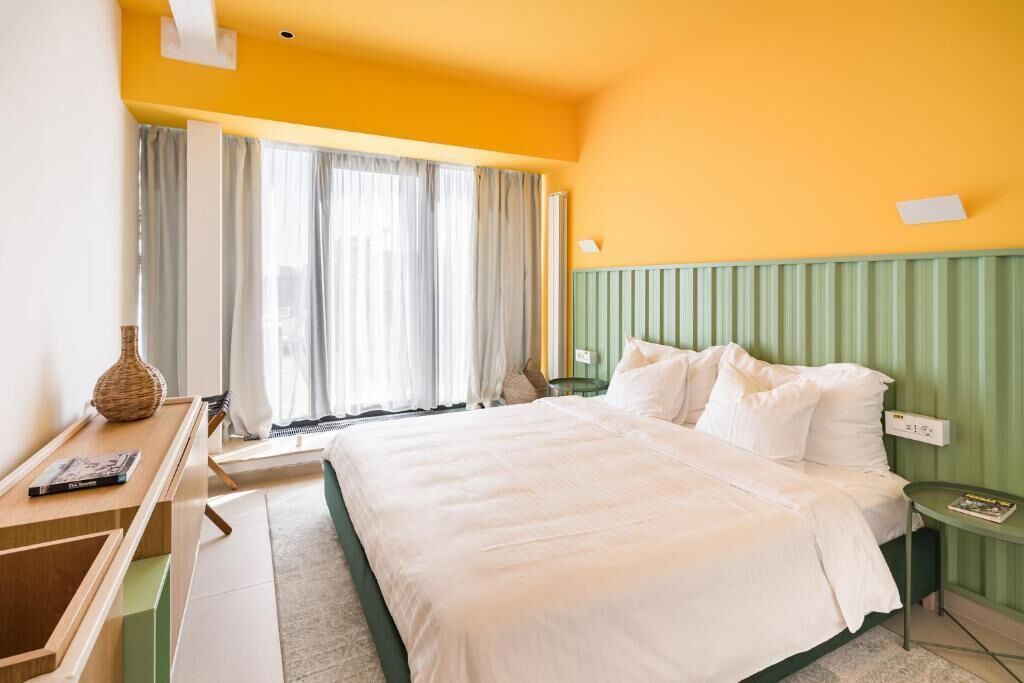 Habitación de hotel con una cama grande, un escritorio con silla, una mesita y una ventana con cortinas.