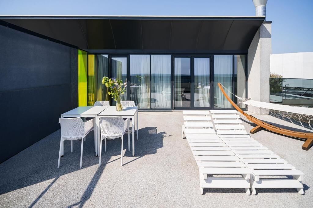 A rooftop terrace with a table and chairs, lounge chairs, and a view of the sea.