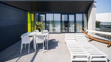 A rooftop terrace with a table and chairs, lounge chairs, and a view of the sea.