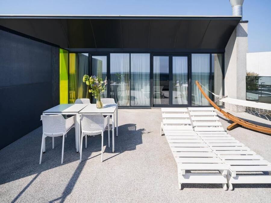 A rooftop terrace with a table and chairs, lounge chairs, and a view of the sea.