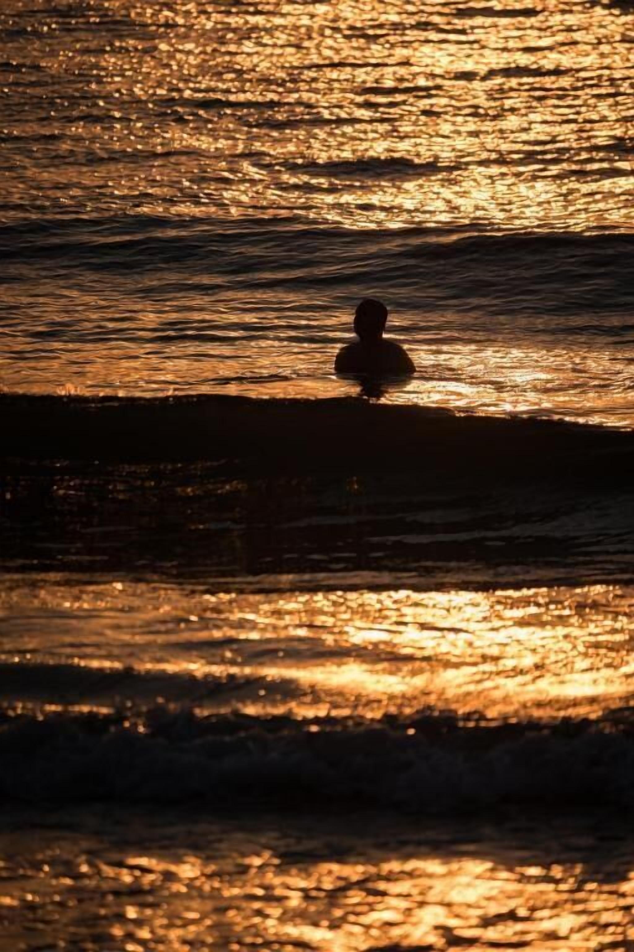 Silueta de una persona de pie en la playa durante el atardecer.