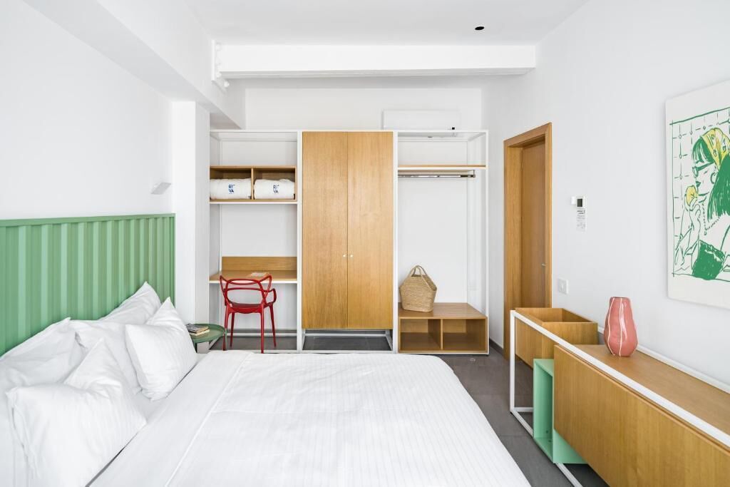 Habitación de hotel con cama, escritorio, silla, armario y una pequeña mesa con un jarrón.