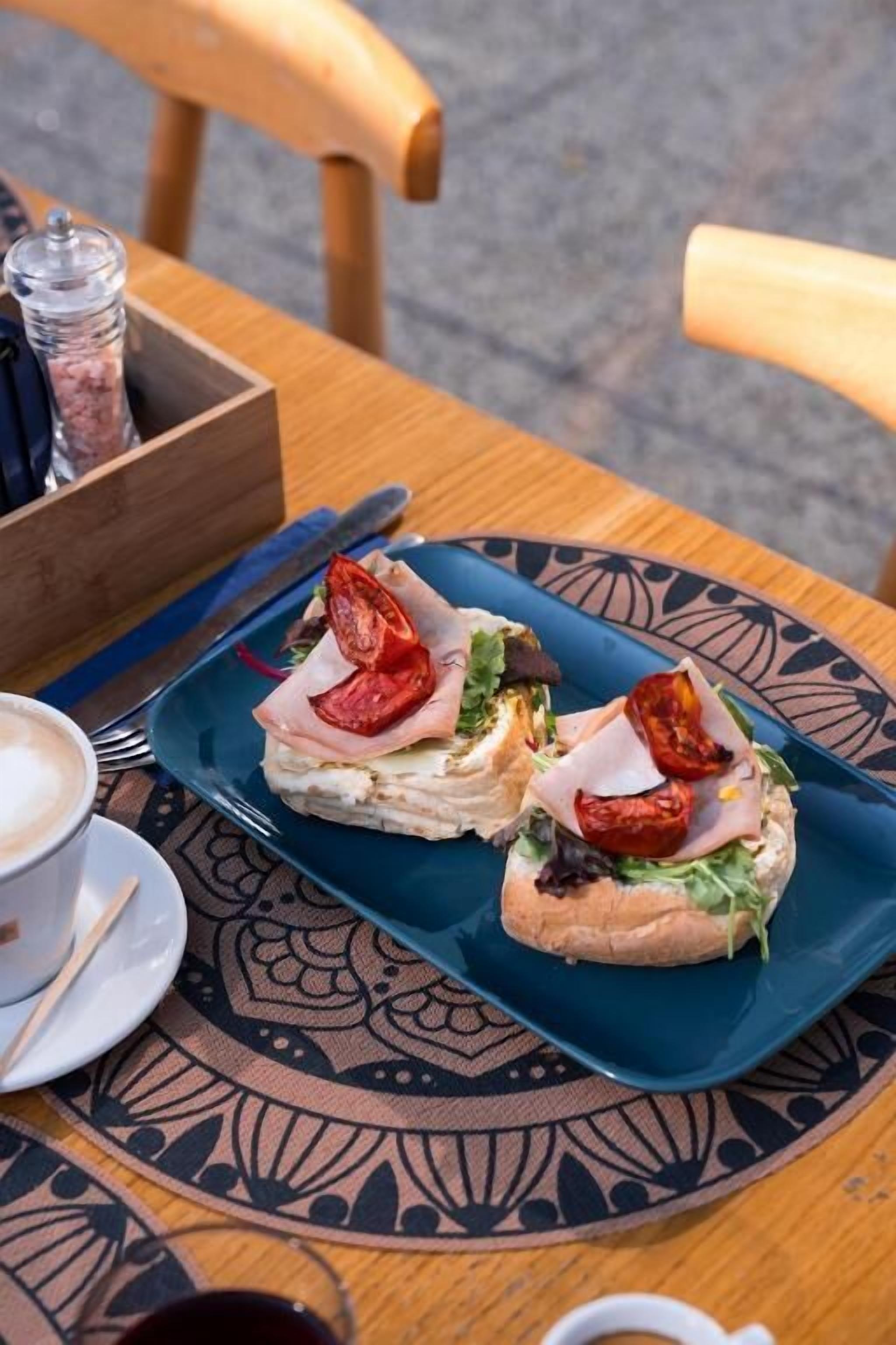 A table with a blue plate containing sandwiches, a cup of coffee, and a small bowl of condiments.