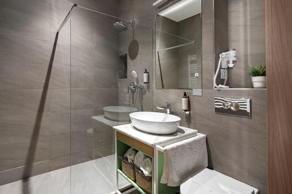 A modern bathroom with a large mirror, a round sink, a showerhead, and a towel rack.