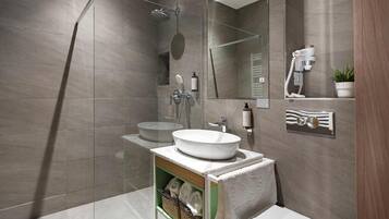 A modern bathroom with a large mirror, a round sink, a showerhead, and a towel rack.