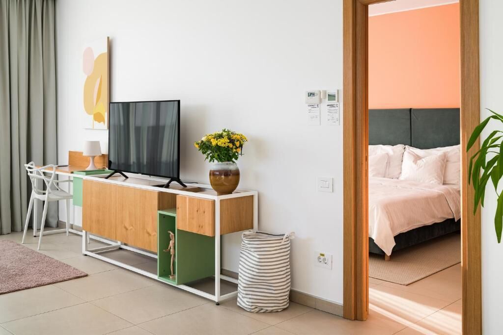 Une chambre d’hôtel moderne équipée d’un lit, d’un bureau avec un ordinateur, d’une télévision et d’une plante.