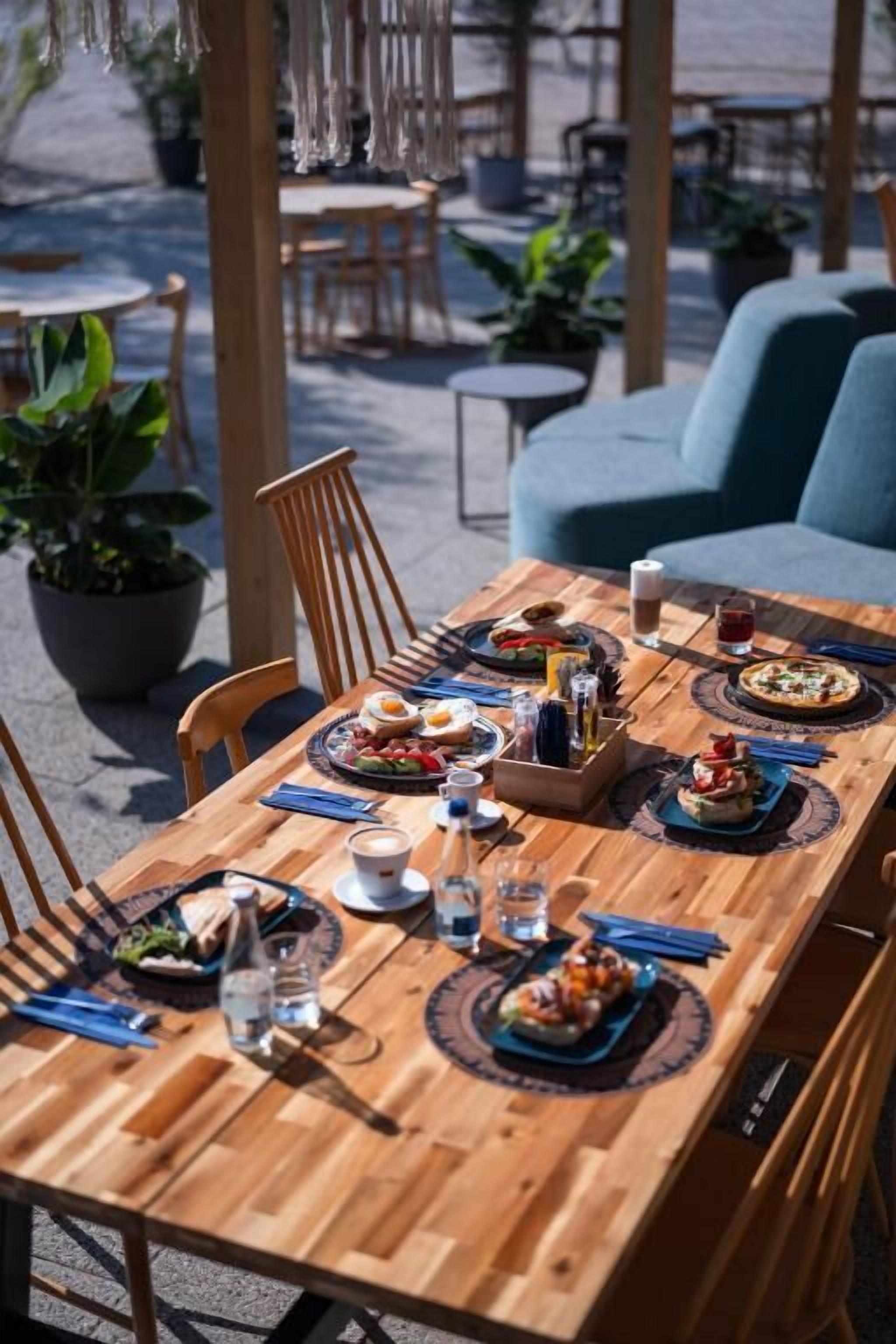 A wooden dining table set with plates, cutlery, and glasses, surrounded by chairs and potted plants.