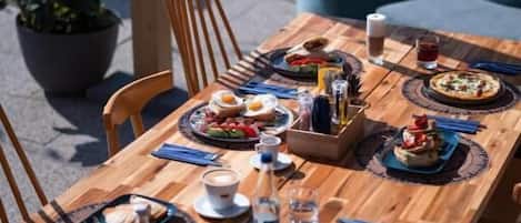 Een houten eettafel, gedekt met borden, bestek en glazen, omringd door stoelen en potplanten.