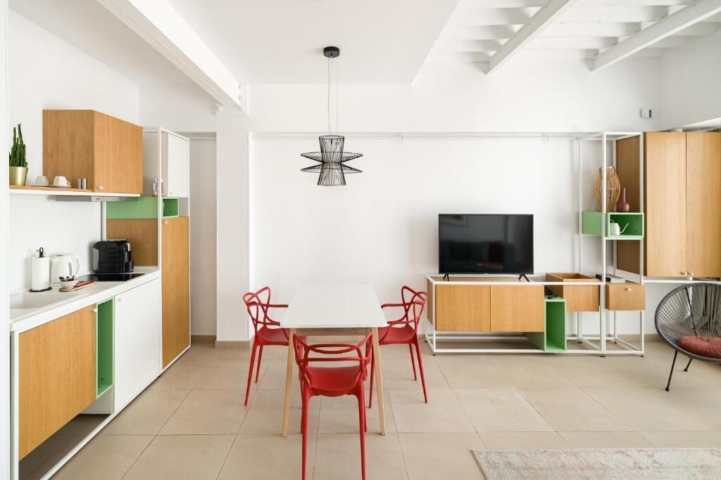 Una cocina moderna con armarios blancos, un comedor con sillas rojas y un televisor en el centro.