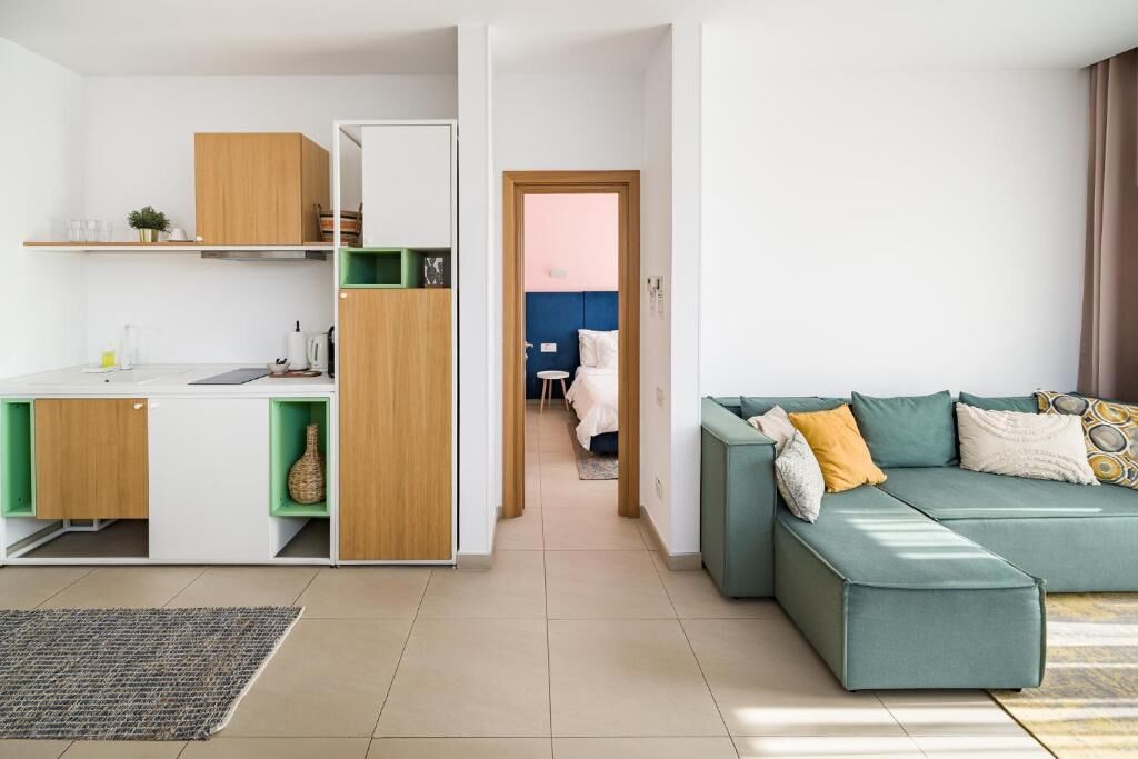 Eine moderne Wohnung mit Küche, einem Wohnbereich mit grünem Sofa und einem durchgegangene Tür erkennbaren Schlafzimmer.