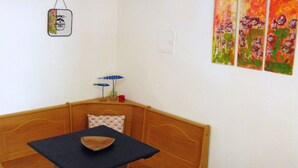 A corner room with a wooden bench, a small table with a bowl, a hanging sign, and three colorful paintings on the wall.
