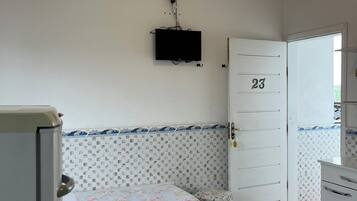 Quarto com duas camas, televisão fixada na parede, porta com o número 23 e parede revestida de azulejos.