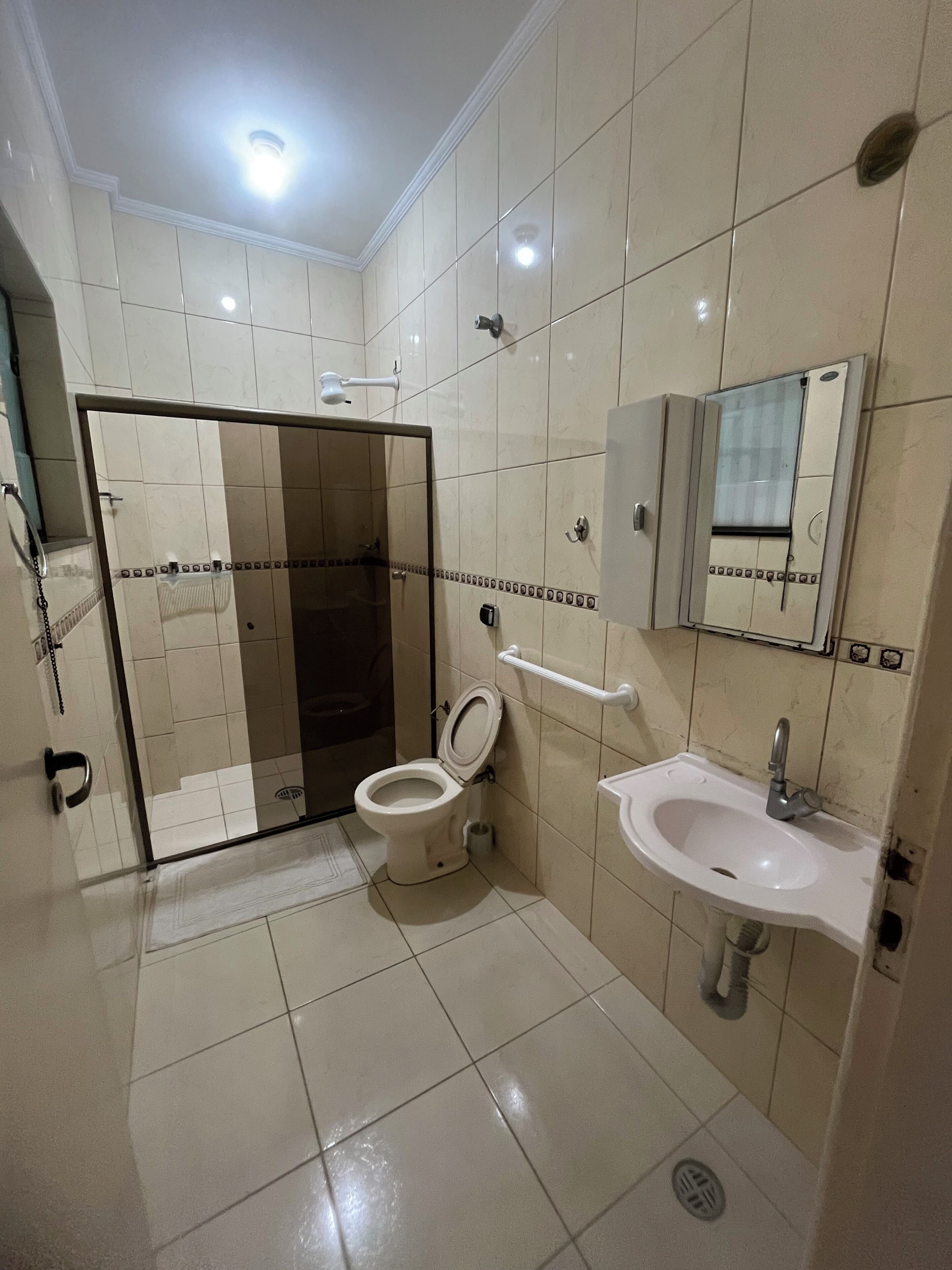 A bathroom with a toilet, sink, shower, and a mirror.