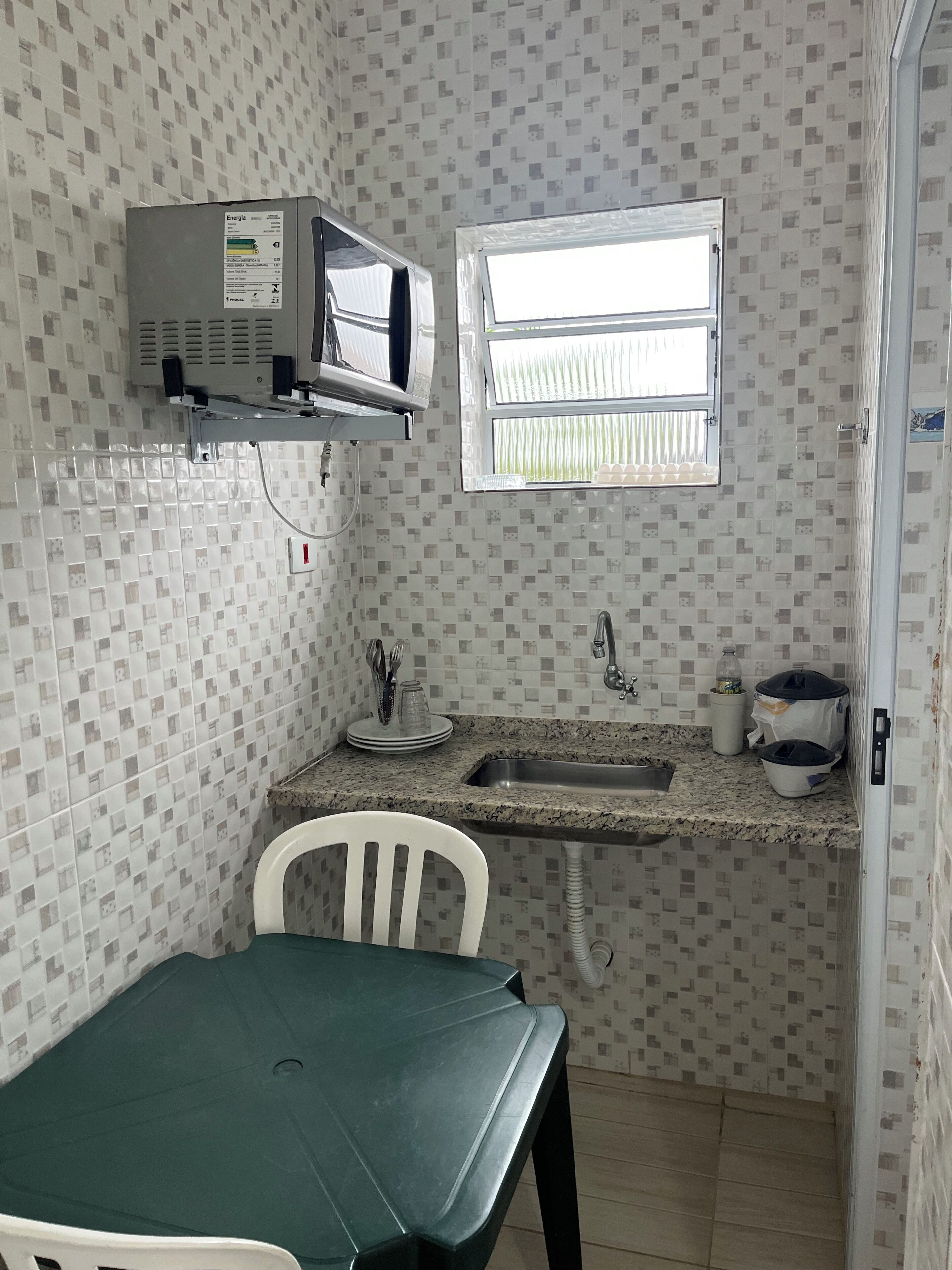 Cozinha compacta com micro-ondas, pia e janela.