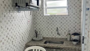 Cozinha compacta com micro-ondas, pia e janela.