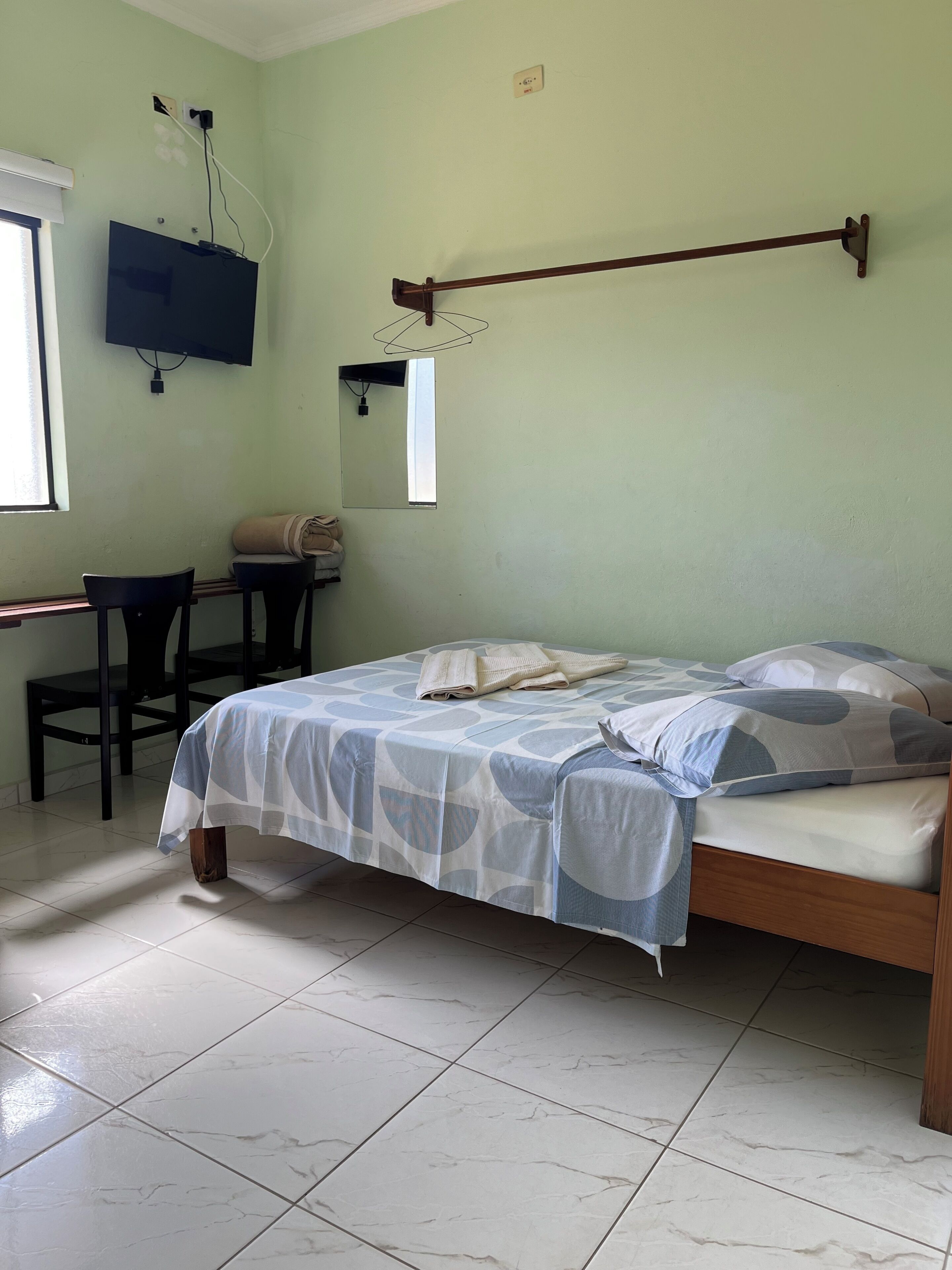 A bedroom with a bed, a desk, a chair, and a television mounted on the wall.