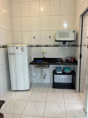 A compact kitchen with a refrigerator, microwave, sink, and a small countertop with dishes and a trash bin. - Park Inn Pesk (Bertioga)