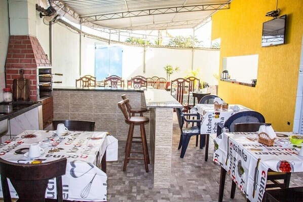 An outdoor dining area with tables covered in tablecloths, chairs, and a brick oven. - Park Inn Pesk (Bertioga)