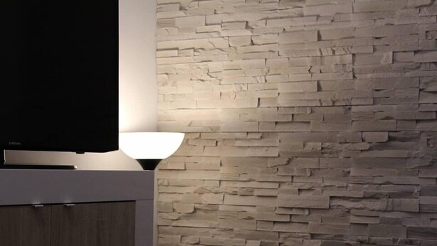 Un interior moderno con pared de textura de piedra, un televisor de pantalla plana y una lámpara de mesa.