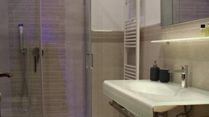 Un baño moderno con ducha envuelta en vidrio, un lavamanos blanco y un perchero.