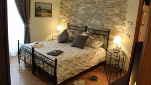 Un dormitorio con pared de piedra, una cama con colcha floral, dos mesitas de noche con lámparas y un cuadro en la pared.