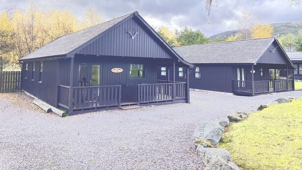 A row of dark wooden cabins with a sign reading "Celtic Lodge." - Braemar Lodge Cabins (Ballater)