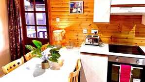 A kitchen with wooden walls, a dining table with chairs, a toaster, and a stove. - Braemar Lodge Cabins (Ballater)