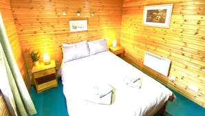 A wooden-paneled room with a bed, bedside tables, a framed picture, and a radiator. - Braemar Lodge Cabins (Ballater)