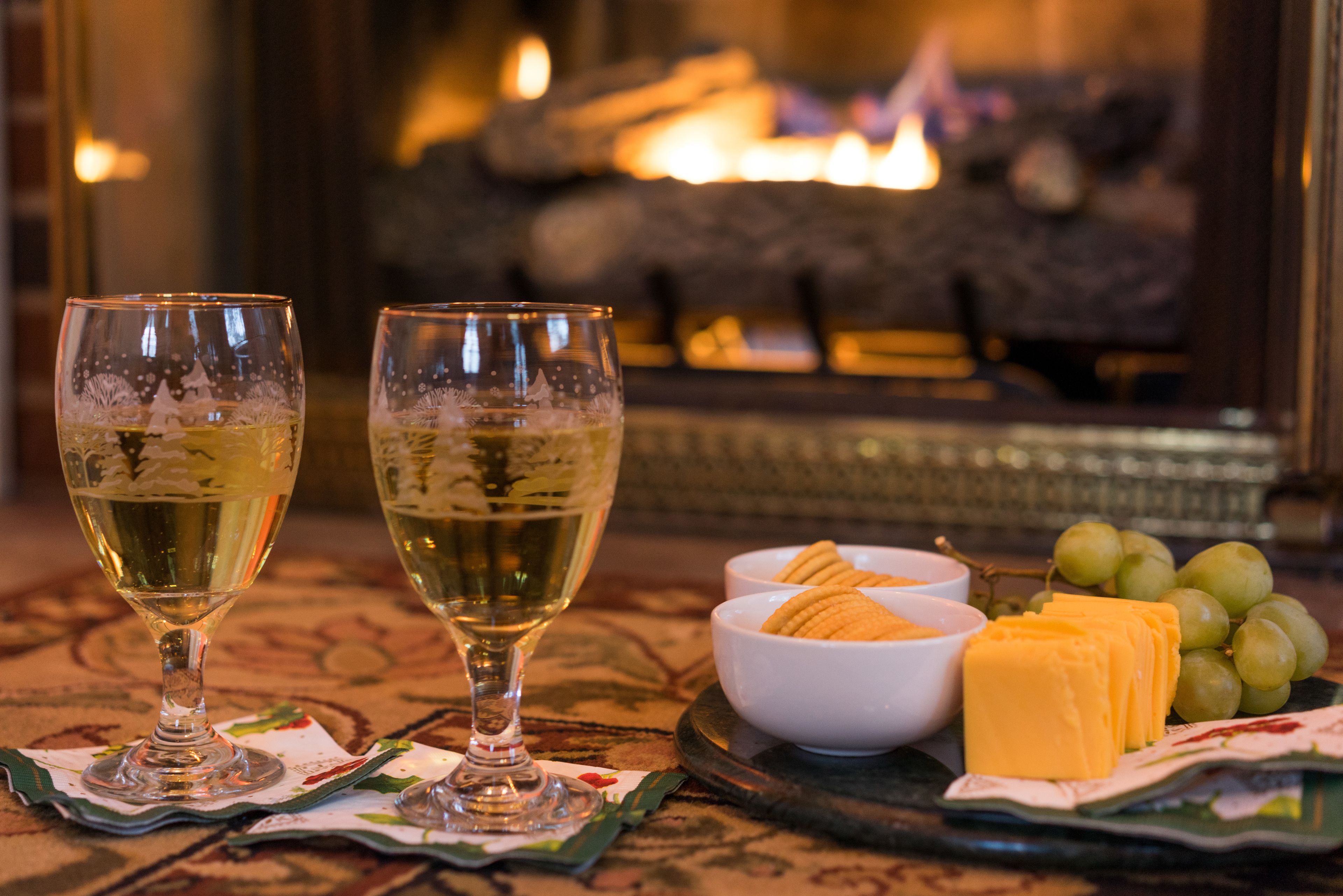 Two glasses of white wine, a bowl of crackers, and a plate with cheese and grapes on a table with a patterned tablecloth.