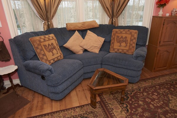 A blue sofa with camel-patterned cushions, a wooden coffee table, and a patterned rug in a room with wooden flooring and a pink wall. - Sutton House B & B (Center Harbor)