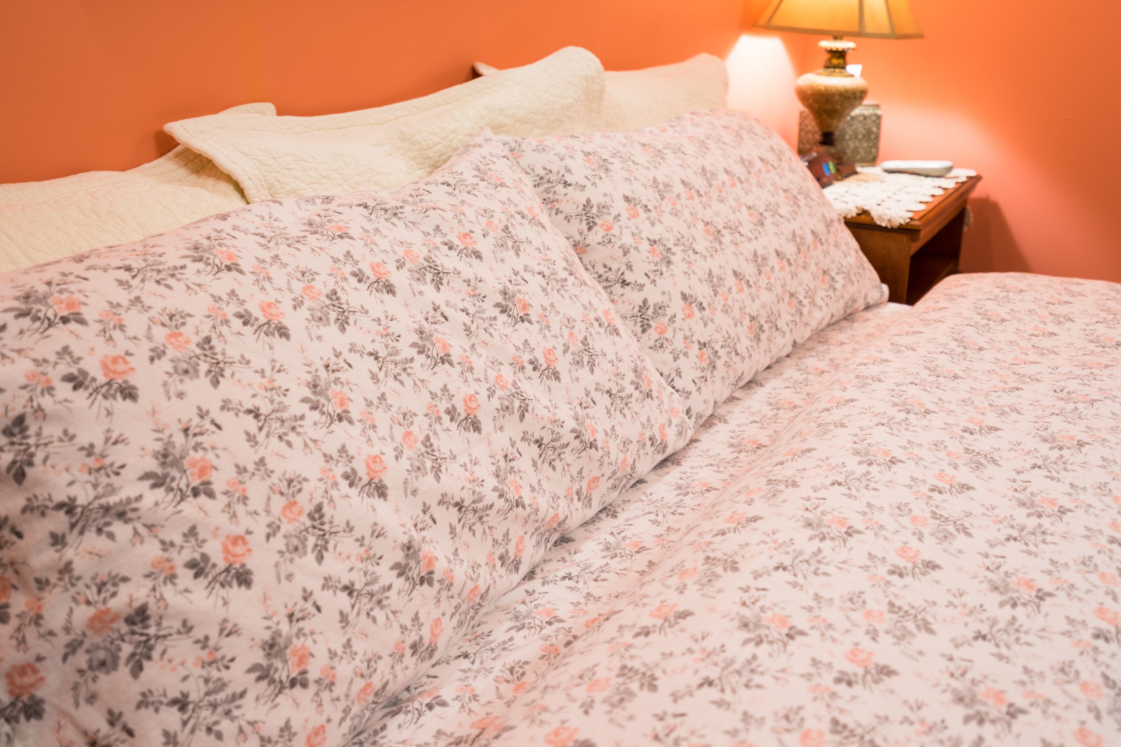 A bed with floral bedding, a bedside table with a lamp, and a wall with a textured pattern.