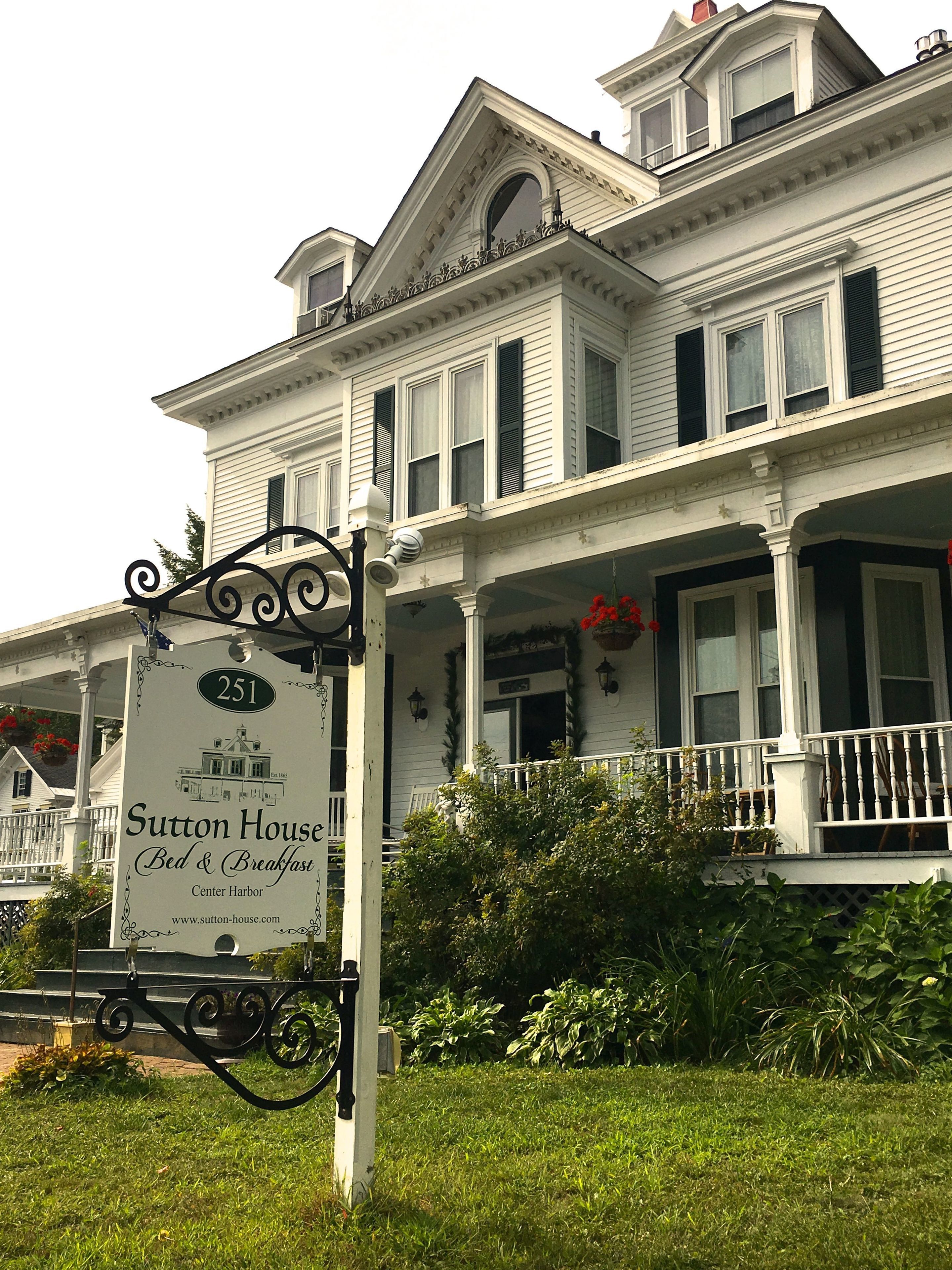A large, white, two-story building with a sign for Sutton House Bed & Breakfast in front.