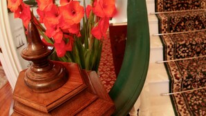 Una escalera con alfombra verde y un jarrón de madera con flores rojas sobre una mesa.