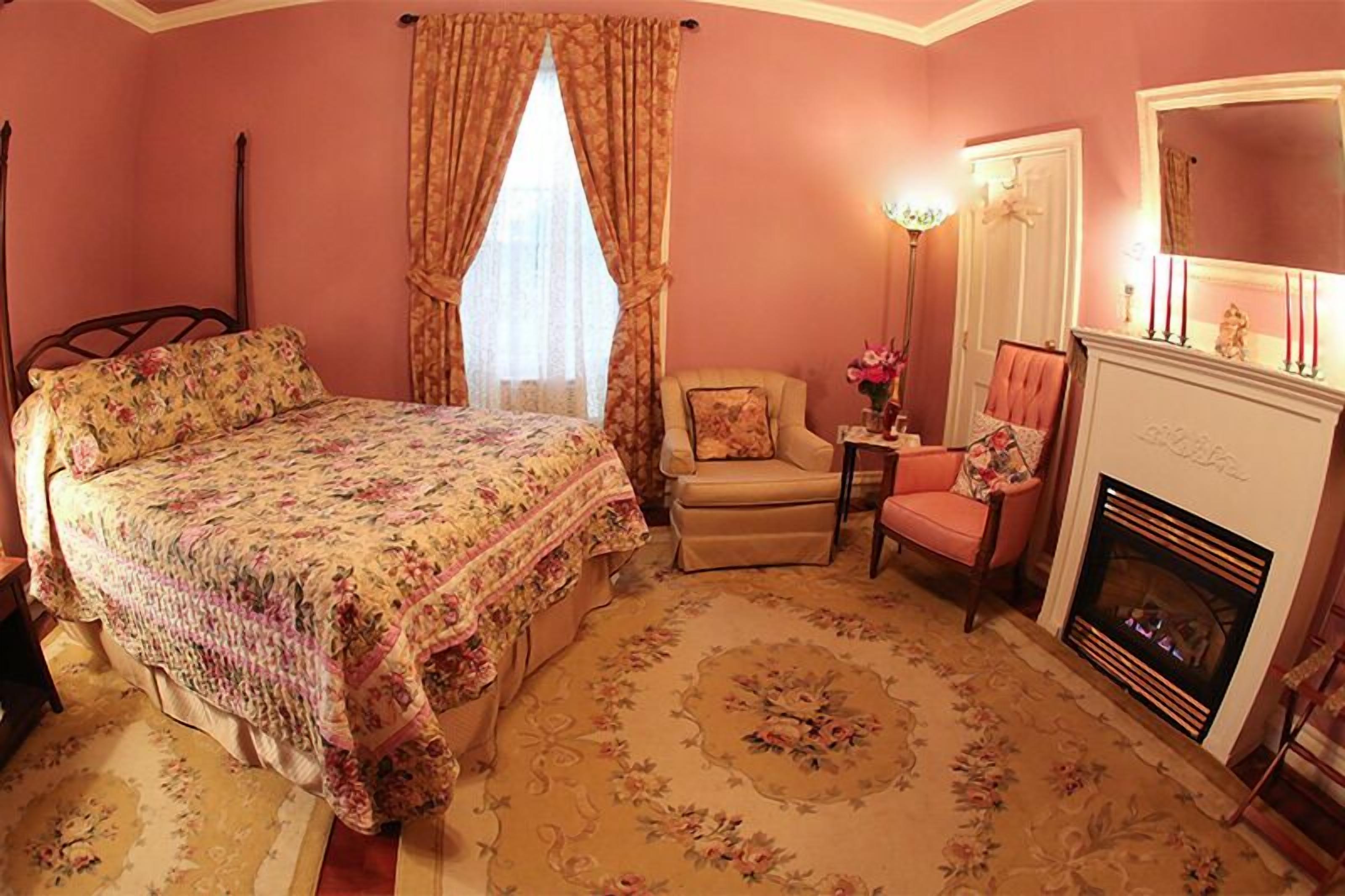 Quarto com cama, cadeira, lareira e espelho.