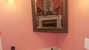 A bathroom with a pink wall, a wooden vanity, a white sink, two wall-mounted lights, a mirror with an ornate frame, and a towel rack with two towels.