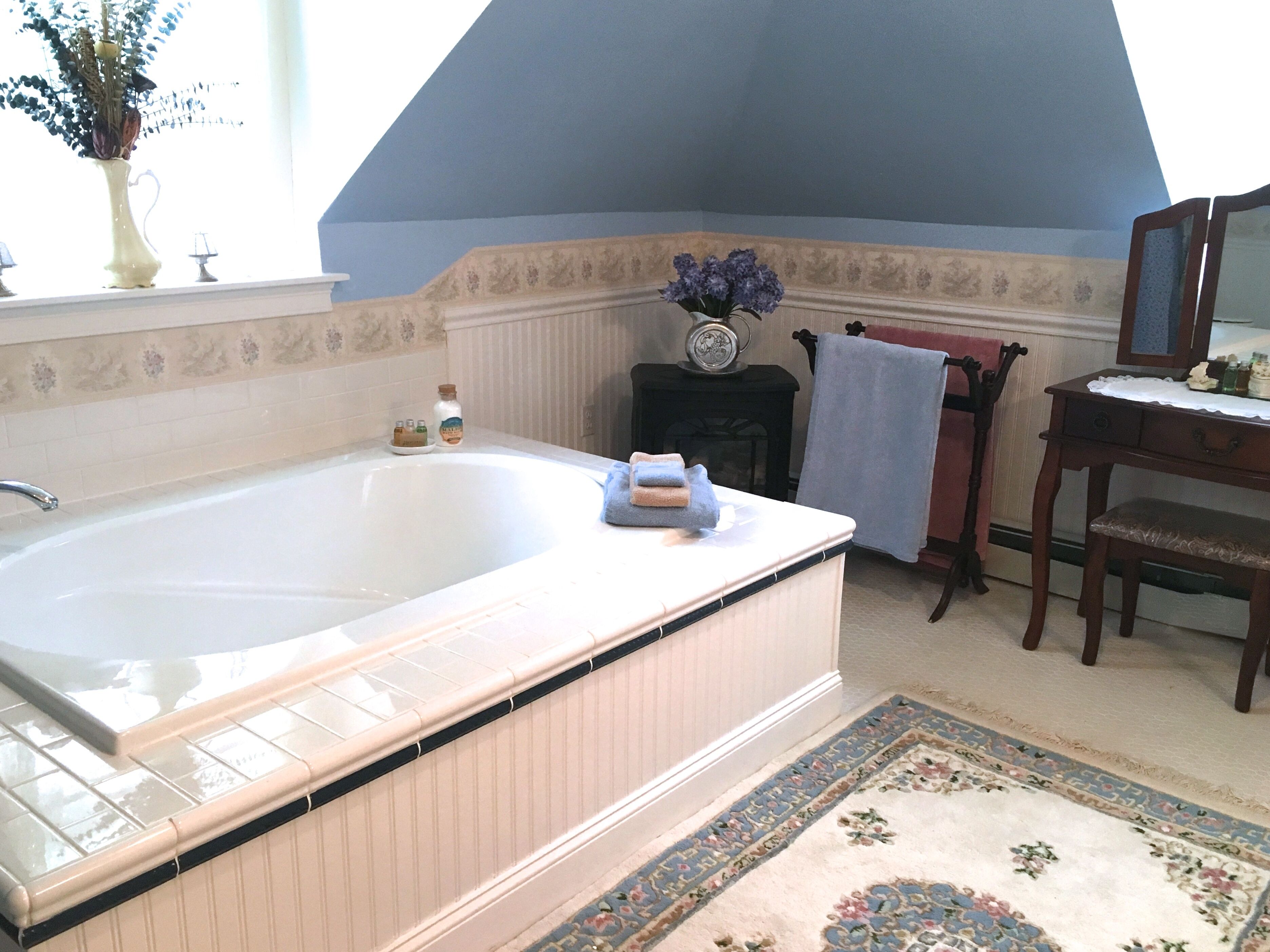 A bathroom with a bathtub, a wooden vanity, a mirror, and a floral rug.
