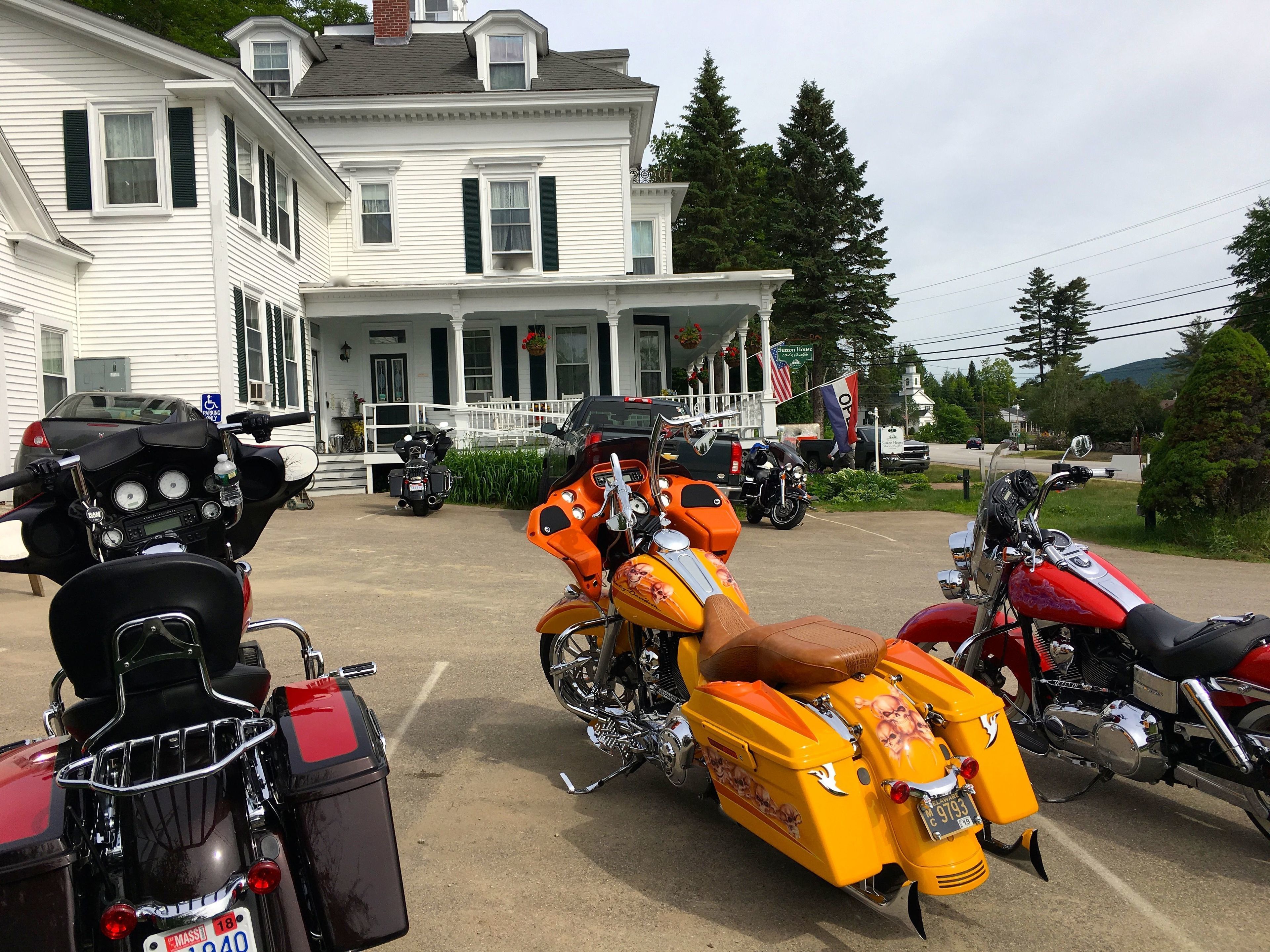 A row of motorcycles parked in front of a white house with a porch.