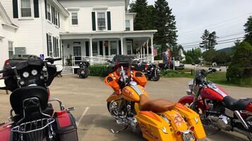 A row of motorcycles parked in front of a white house with a porch.