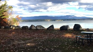 Zona de picnic junto al lago con bancos y una mesa, rodeada de rocas y árboles.