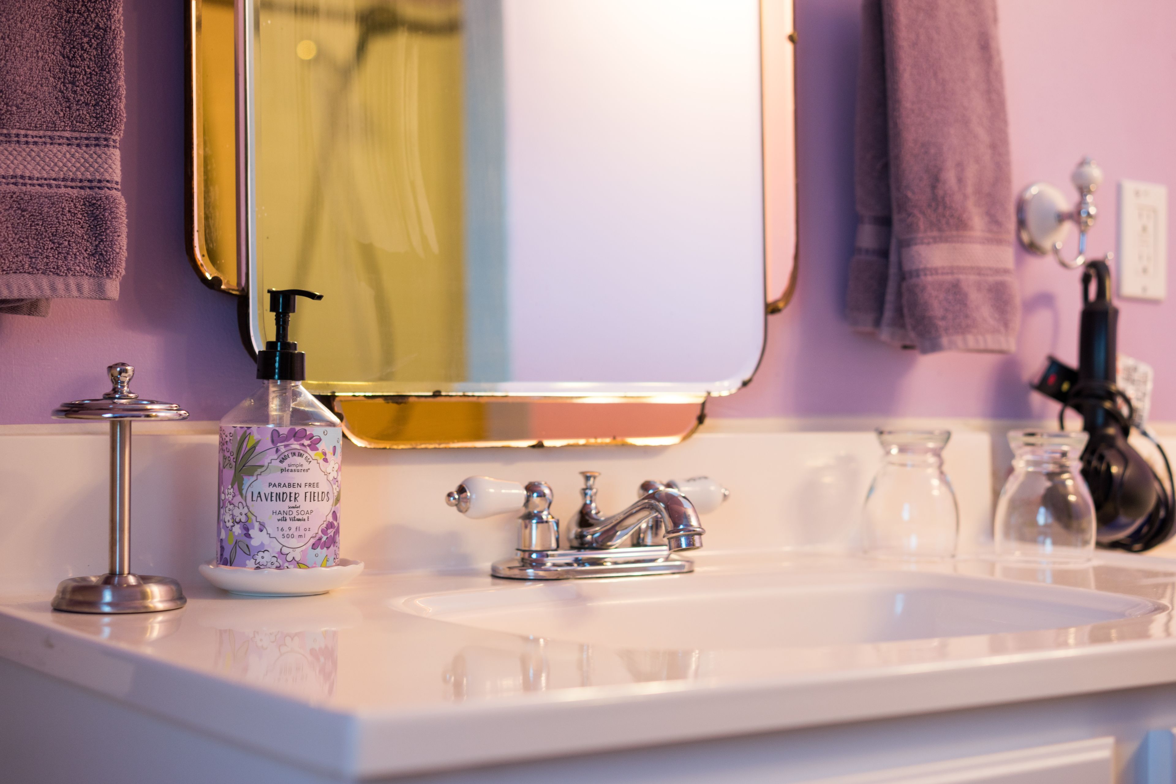 A bathroom sink with a mirror, a lavender fields hand soap dispenser, and a faucet.
