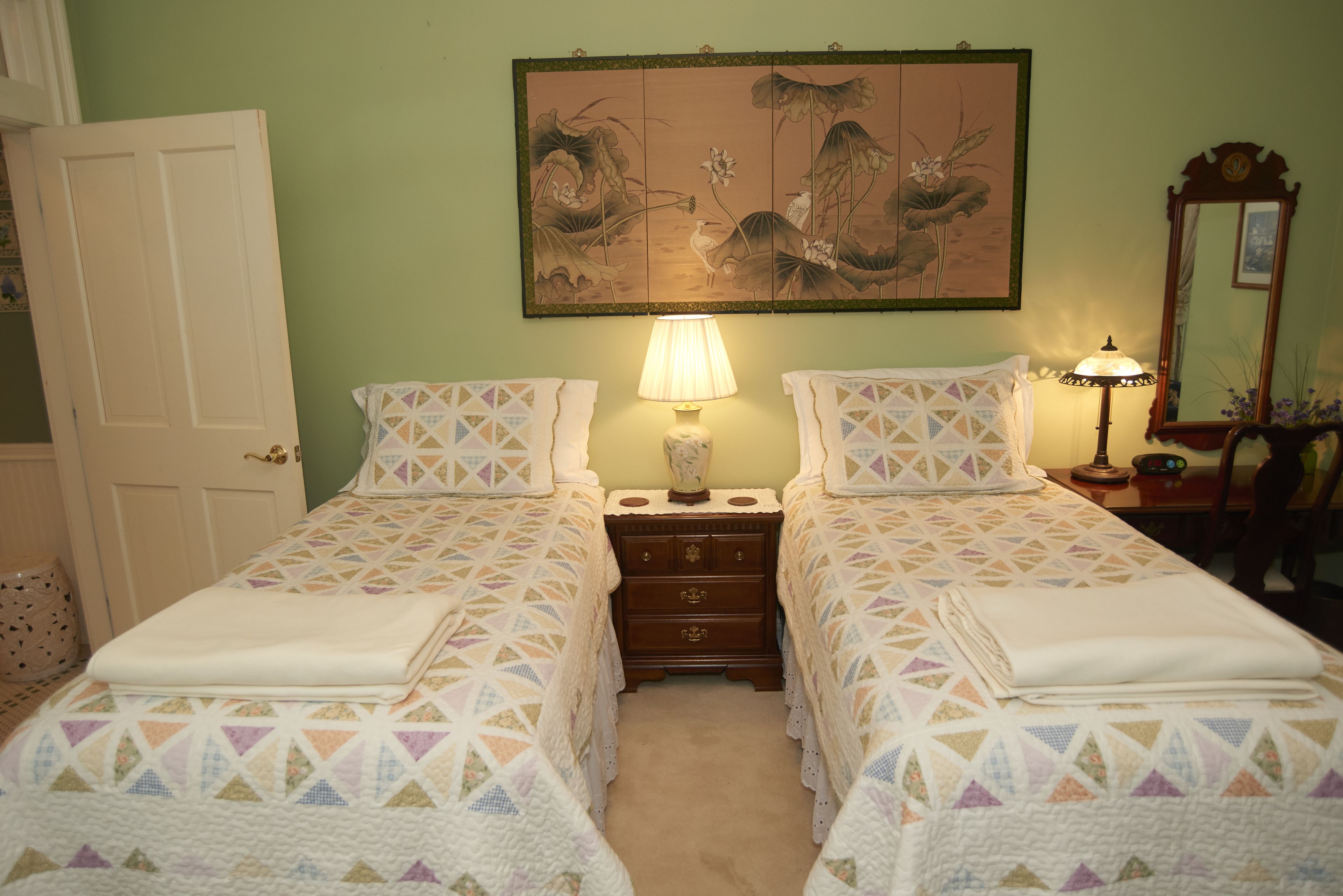 Een slaapkamer met twee bedden, een nachtkastje, een lamp, een spiegel en een schilderij aan de muur.