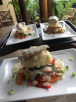 Una mesa de comedor con dos platos blancos cuadrados de comida, cada uno coronado con un trozo de pescado y vegetales, y una bandeja con más platos.