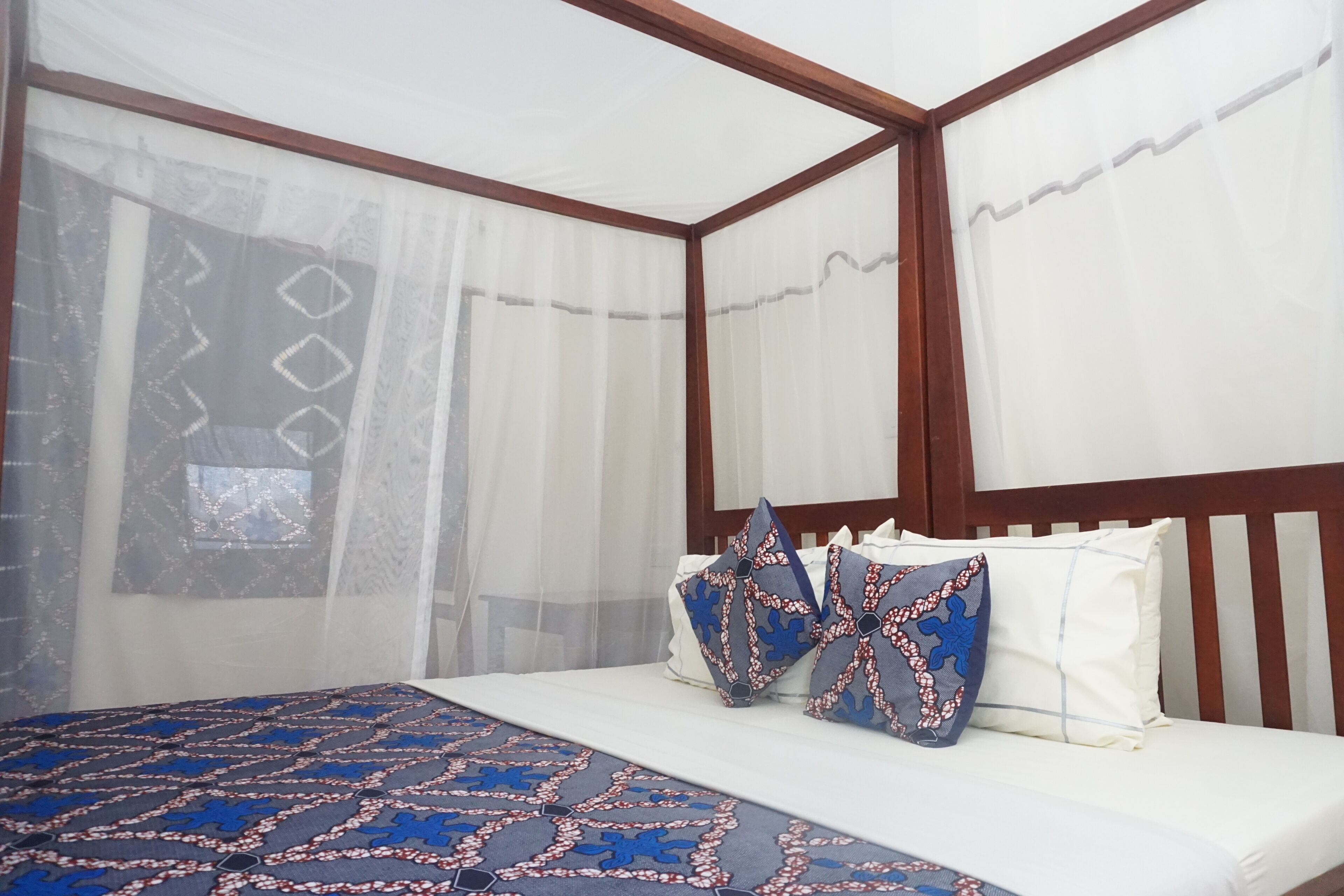 A bedroom with a canopy bed, white bedding, and decorative pillows.