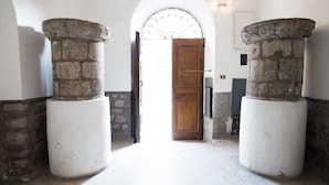 A corridor with two stone columns, a wooden door, and a white wall with a circular window. - Le Erbe Guest House (Viterbo)