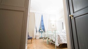 A bedroom with a bed, a chair, a small table, and a window with curtains. - Le Erbe Guest House (Viterbo)