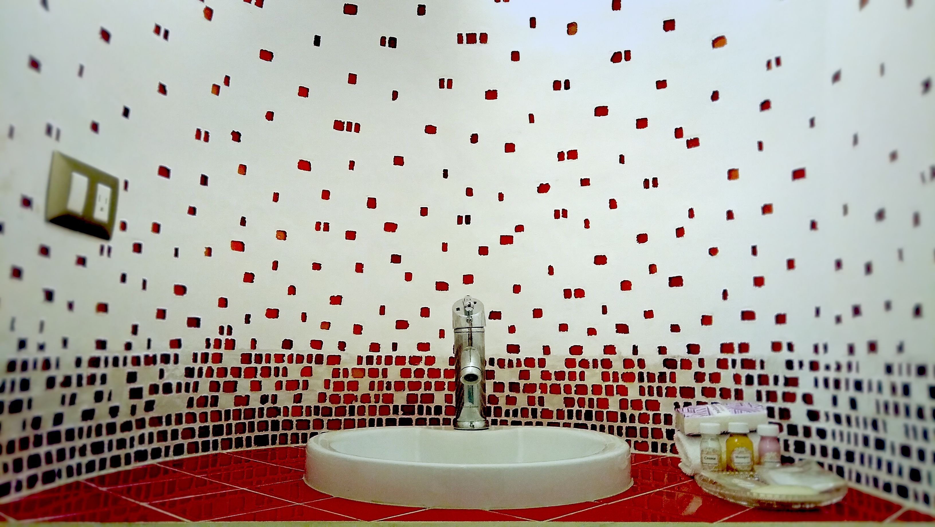 A bathroom with a white sink, red and white mosaic tiles on the walls, and a red floor.